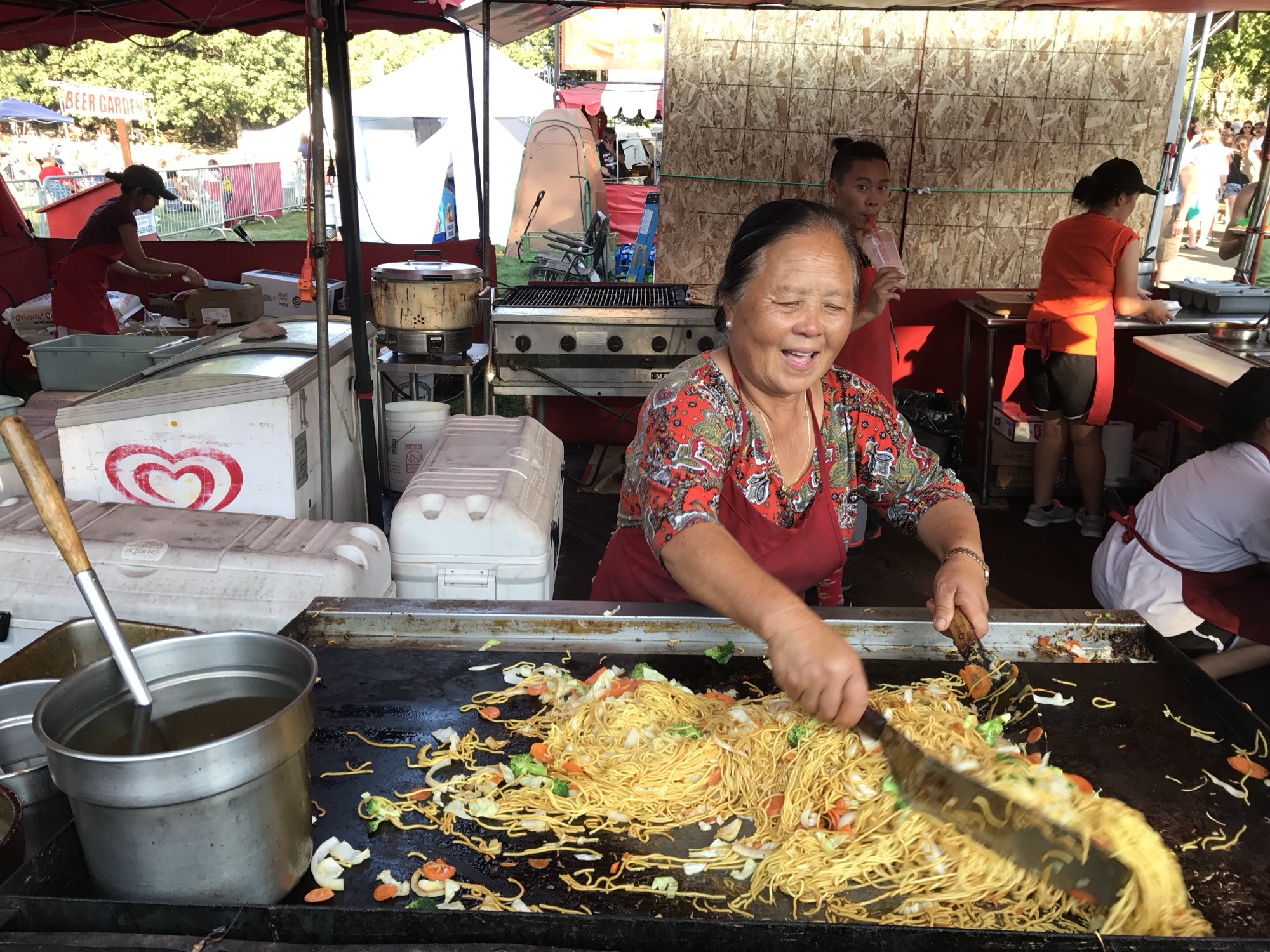 A cook laughing as she works a griddle piled high with noodles and vegetables at a Pig Out in the Park food booth.